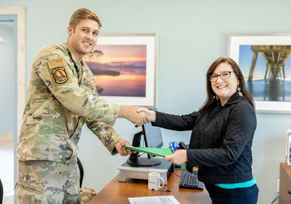 A man in military uniform shakes hands with a woman in a black jacket.