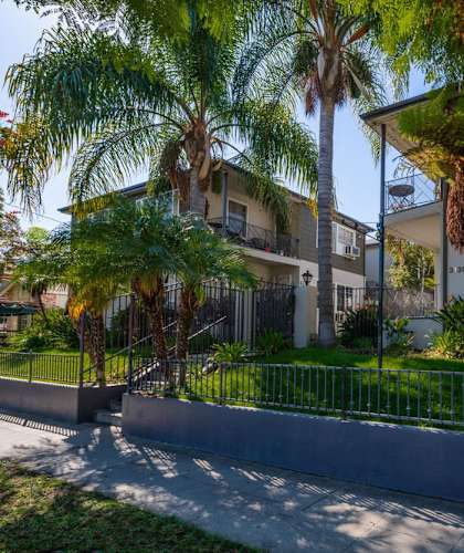 A residential area with a house, palm trees, and a fence.