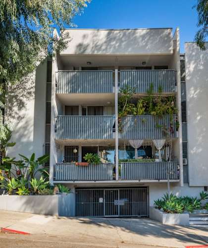 A modern building with balconies and plants in front.