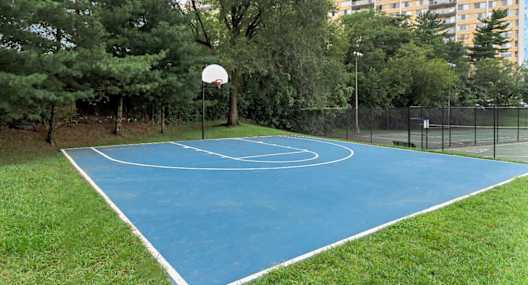 A basketball court surrounded by trees and a tall building in the background.