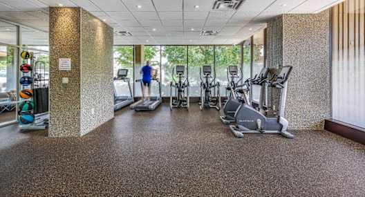 A gym with treadmills, elliptical machines, and a person walking in the background.