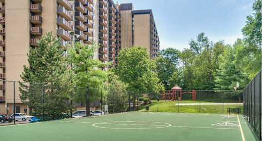 A basketball court is surrounded by apartment buildings and trees.