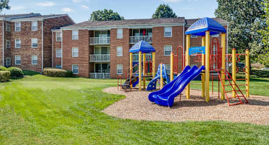 A playground with a blue slide and red ladder in front of a brick building.