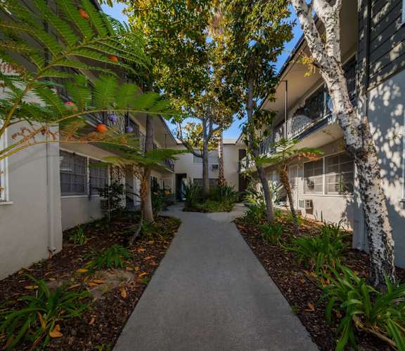 A concrete walkway leads through a landscaped courtyard between two buildings.