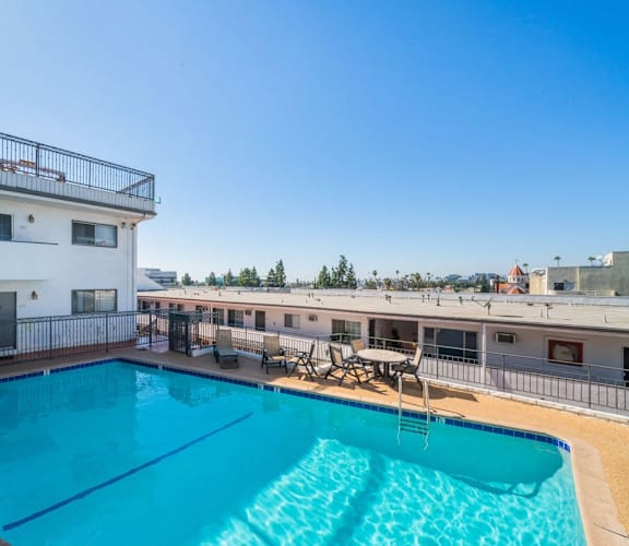 A swimming pool in a sunny day surrounded by apartment buildings.