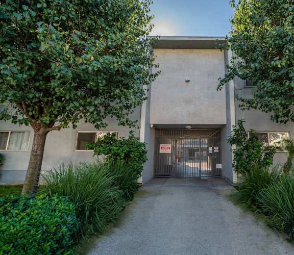 A concrete building with a gate in the middle of a pathway flanked by trees.