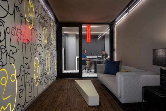 Two people are sitting at a table in a room with a neon sign on the wall.