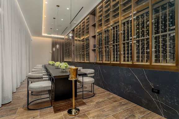 A long table with chairs and a vase of flowers is in front of a wine rack.