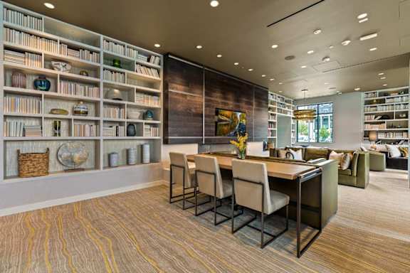 A room with a long table and chairs with a bookshelf on the wall.