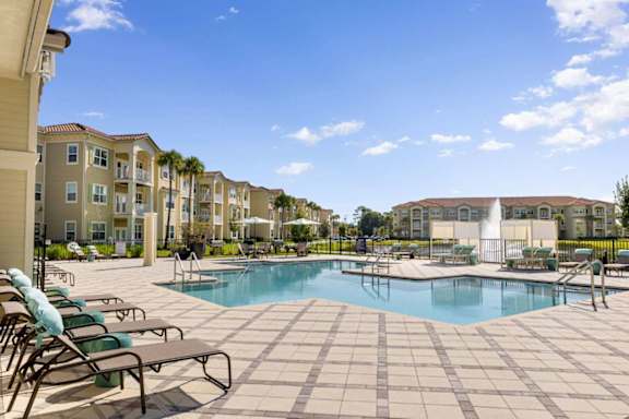 A swimming pool surrounded by lounge chairs and umbrellas in front of apartment buildings.