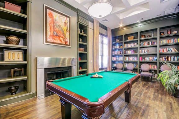 A pool table in a room with a fireplace and bookshelves.