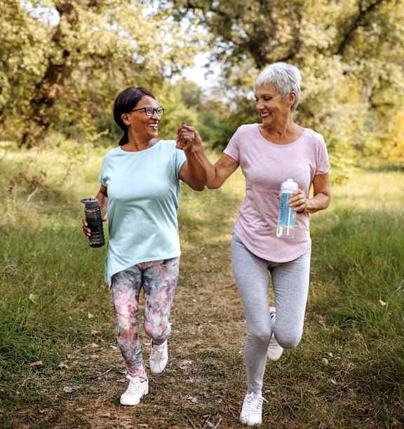 Two women jogging in a grassy area.