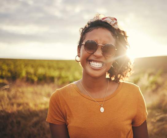a woman in an orange shirt and sunglasses stands in a field with the sun shining on her at The Legend, Waco