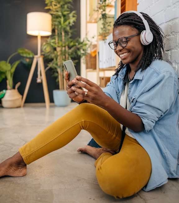 a woman sitting on the floor wearing headphones and looking at her cell phone