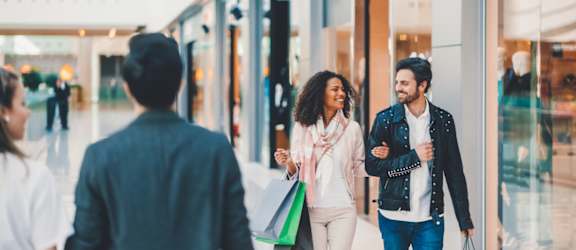 A man and a woman are walking hand in hand in a mall.