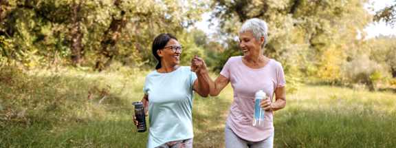 Two women jogging in a grassy area.