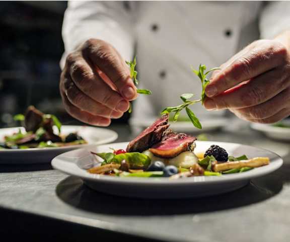 A chef is garnishing a plate of food with herbs at Ophelia on Queen Apartments, Kitchener, ON, N2G 0E7