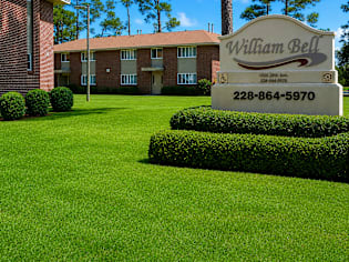 A sign for William Bell stands in front of a building and trees.