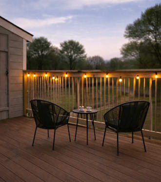 Two chairs and a small table are on a deck with lights strung up on the fence.
