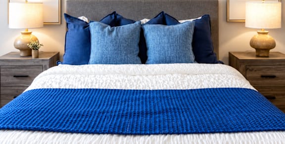 A bed with a blue comforter and pillows is flanked by two lamps on nightstands.