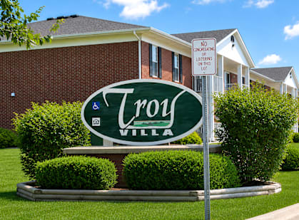 A sign for Troy Village is displayed in front of a brick building.