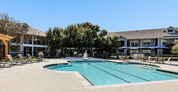 A large outdoor swimming pool with lounge chairs and trees in the background.