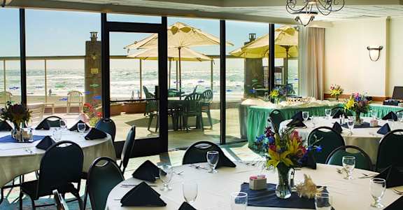 A dining room with tables set for a meal with a view of the beach outside.