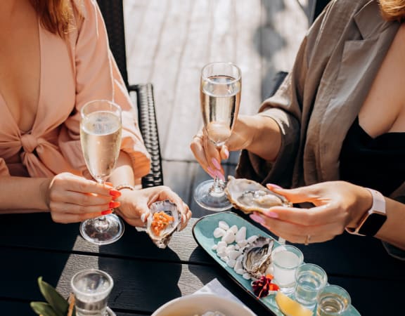 three women sitting at a table with plates of oysters and glasses of champagne