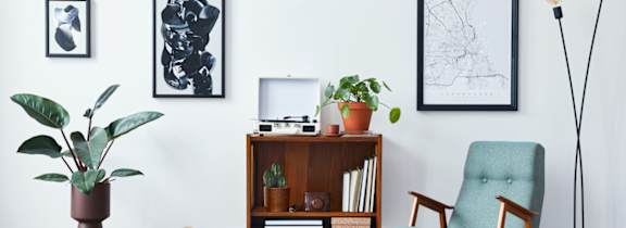 A living room with a chair, a plant, a lamp, and pictures on the wall.