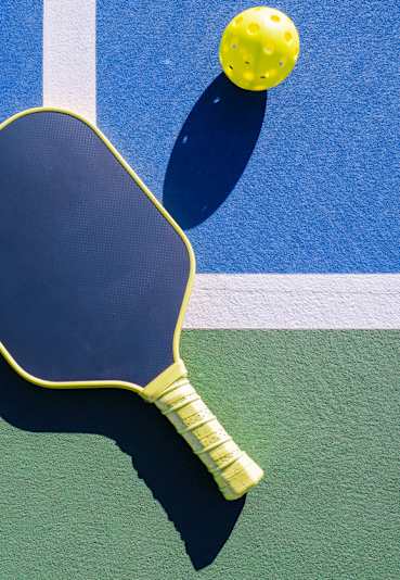A yellow and black paddle is on a tennis court with a ball in the air.