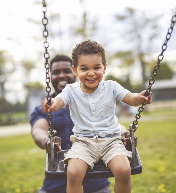 a little boy sitting on a swing with his father in the park at Tara Oaks in Houston, TX