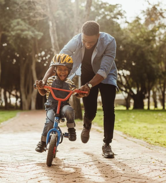 a man helping a young boy ride a bike at Cambridge Village in Houston, TX