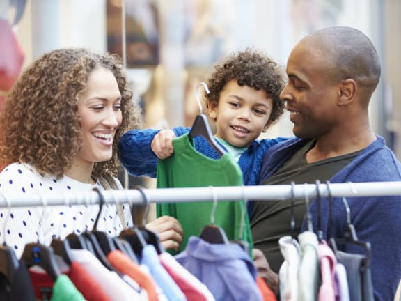 a man and woman with a young child looking at clothes on a rack in a store