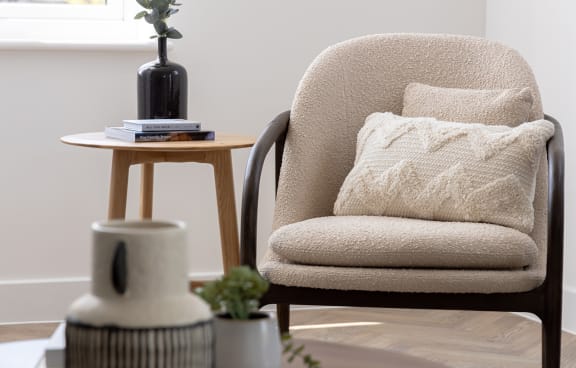a chair with a pillow next to a table with a vase and a book