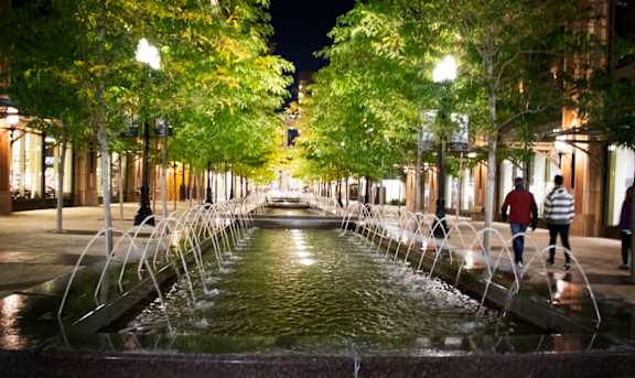 A fountain in the middle of a city street at night.
