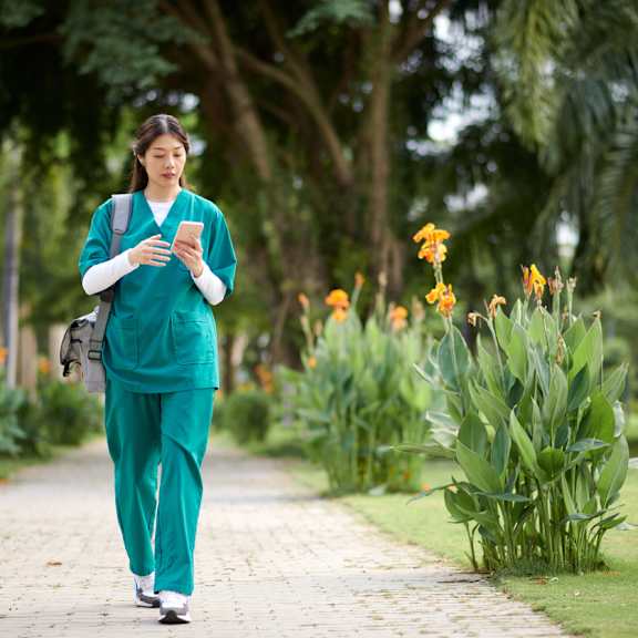 A woman in scrubs walks down a path in a park. at Park Lamont Apartments & Townhomes, Ohio