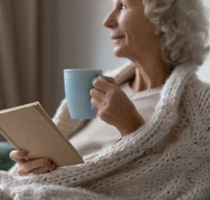 A woman with a book and a cup in her hands is wearing a white sweater.