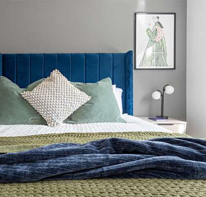 A bed with a blue headboard and a green blanket.