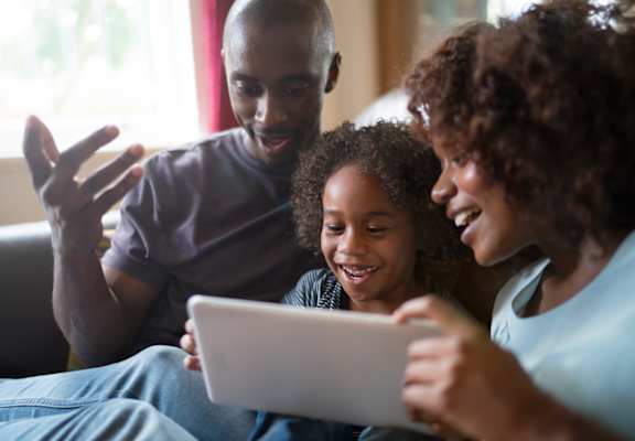 a family sitting on a couch looking at a tablet