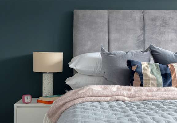 A bed with a grey headboard and a pink blanket.