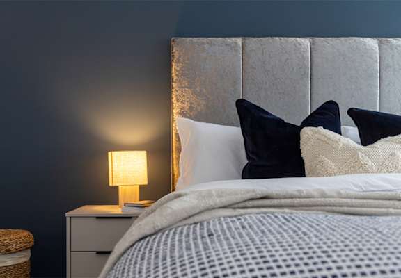 A bed with a white comforter and a lamp on a nightstand.