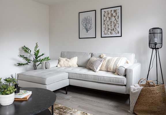A living room with a white couch, a black table, and two framed pictures on the wall.
