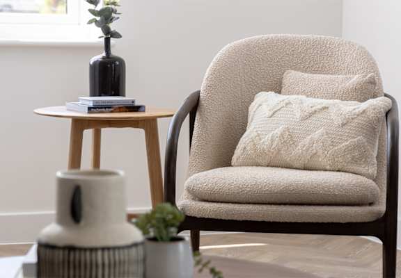 a chair with a pillow next to a table with a vase and a book