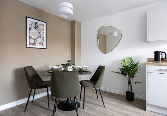 A dining room with a table set for two and a potted plant.