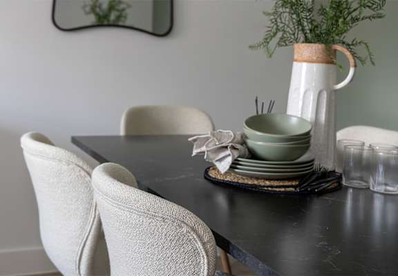 A table with a black top has a white vase with a green plant in it and a stack of green dishes.