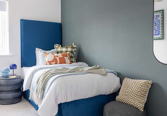 A bed with a white comforter and a blue headboard with a pillow and a blanket on it.