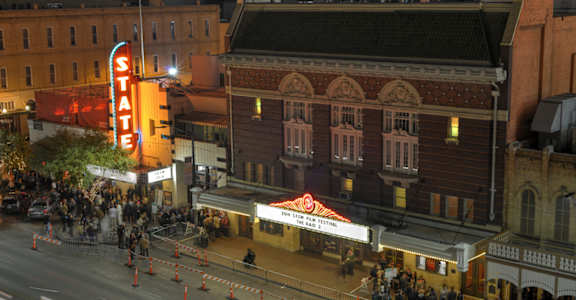 a city street at night with people walking around and a theater sign in the background