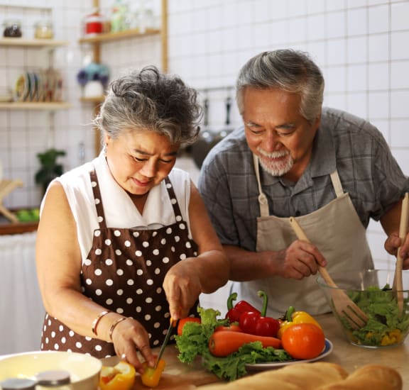 an elderly couple in the kitchen preparing a salad