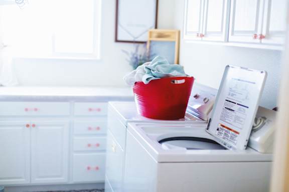 A red bucket with a cloth in it is on top of a white washing machine.