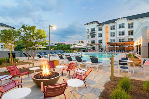 a patio with a fire pit and chairs around a pool